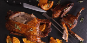 Cutting the roast duck and oranges on a slate board. Horizontal top view